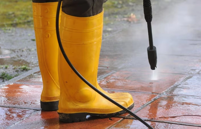 person-wearing-yellow-rubber-boots-with-high-pressure-water-nozzle-cleaning-dirt-tiles