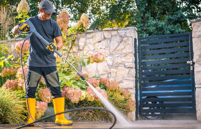 worker-yellow-boots-using-pressure-washer-clean-patio-outside-garden-gate-afternoon
